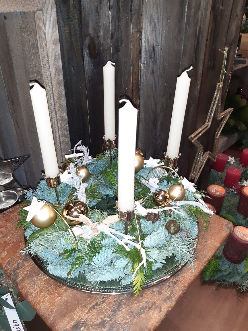 Ein Adventskranz mit weißen Kerzen, grünen Zweigen und goldenen Kugeln