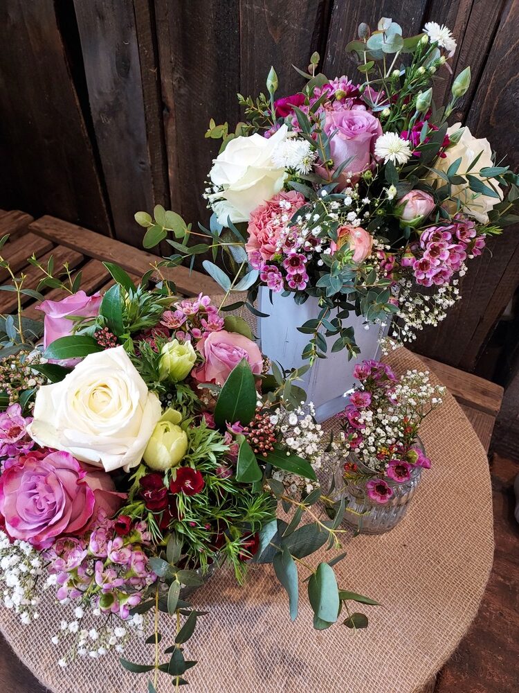 Zwei Blumenarrangements mit Rosen in Rosa, Weiß und Grün auf Holztisch.