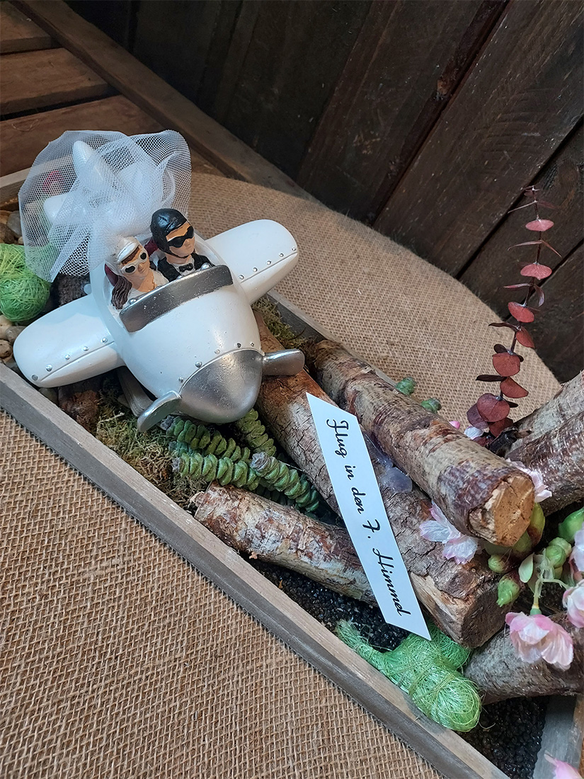 Ein Hochzeitspaar aus Keramik fliegt in einem weißen Flugzeug aus Holz.