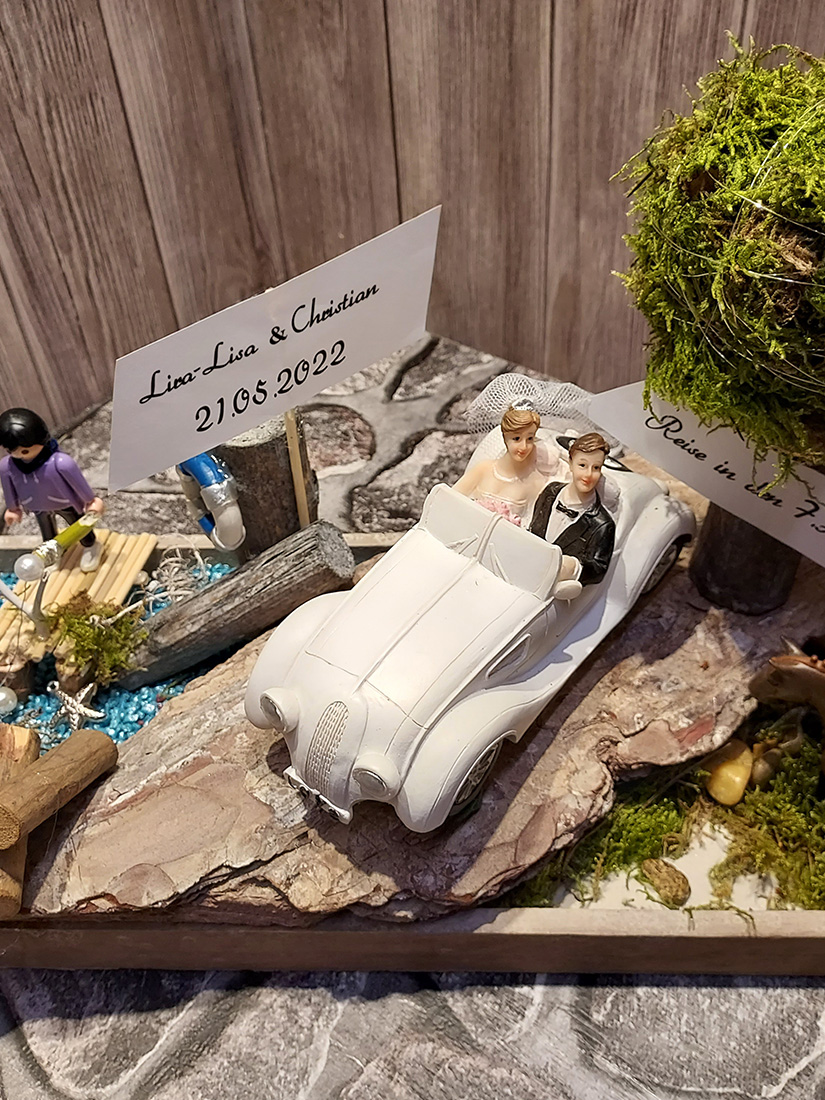 Miniaturbrautpaar in weißem Cabrio auf rustikaler Tischdeko mit Moos und Schild
