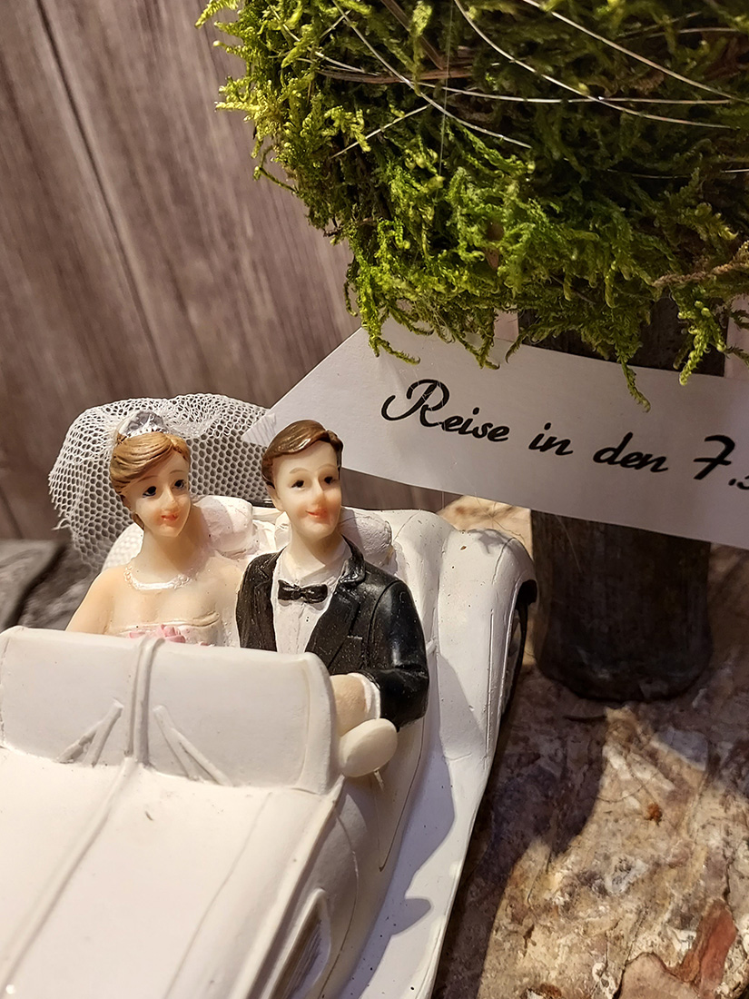 Ein Brautpaar aus Porzellan lächelt fröhlich in einem weißen Auto.