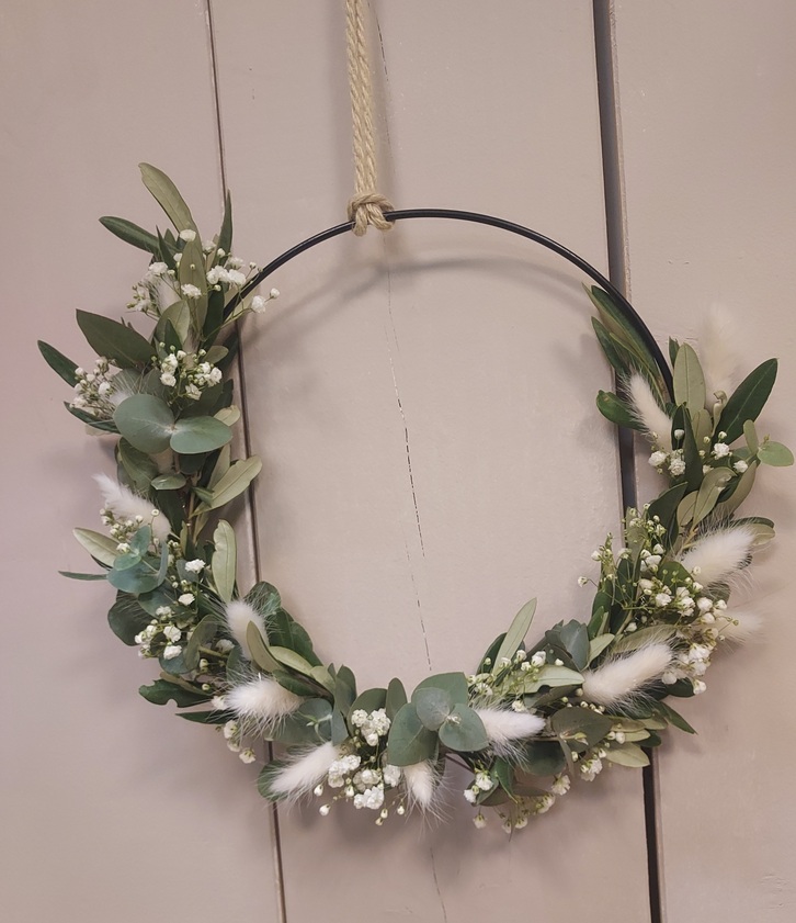 Ein grüner Kranz mit weißen Blumen und Federn hängt an einem Seil.