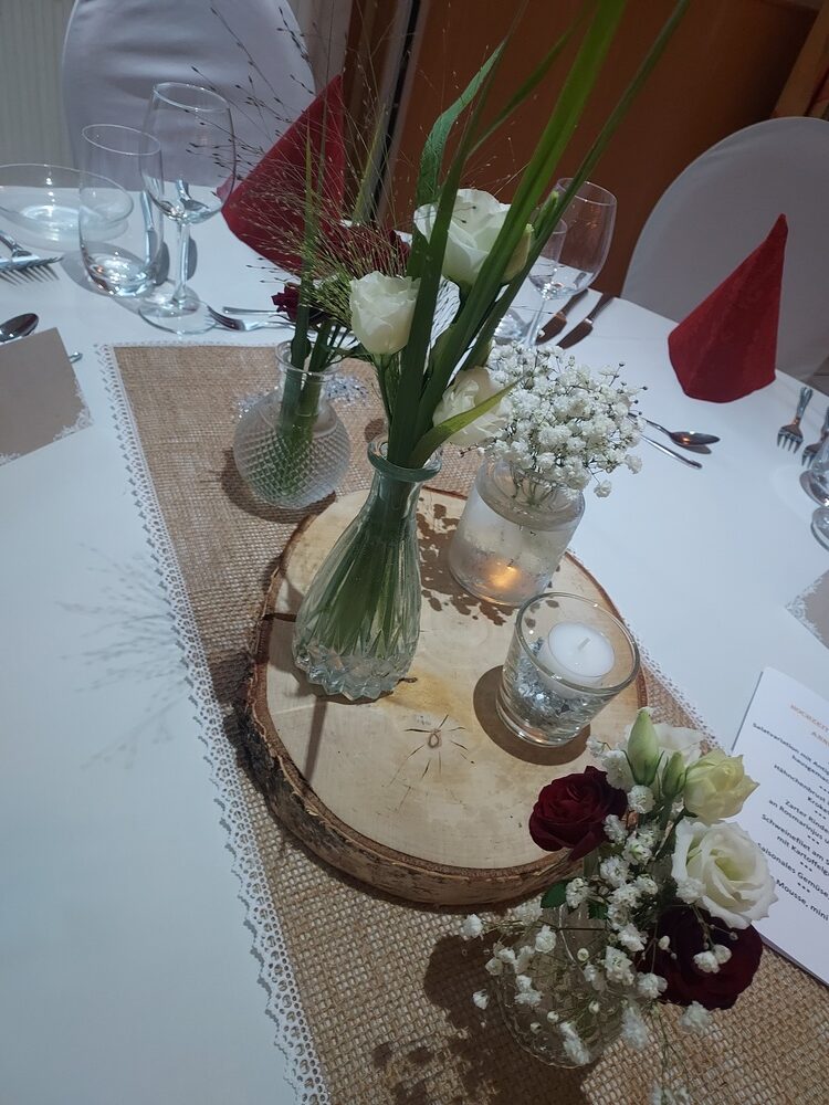 Ein eleganter Tisch mit weißen Rosen, Kerzen und roten Servietten.