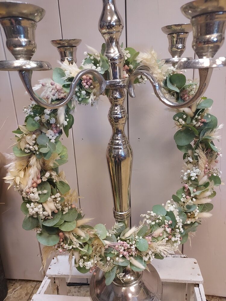 Silberner Kerzenleuchter mit Blumenkranz aus Eukalyptus und Schleierkraut.