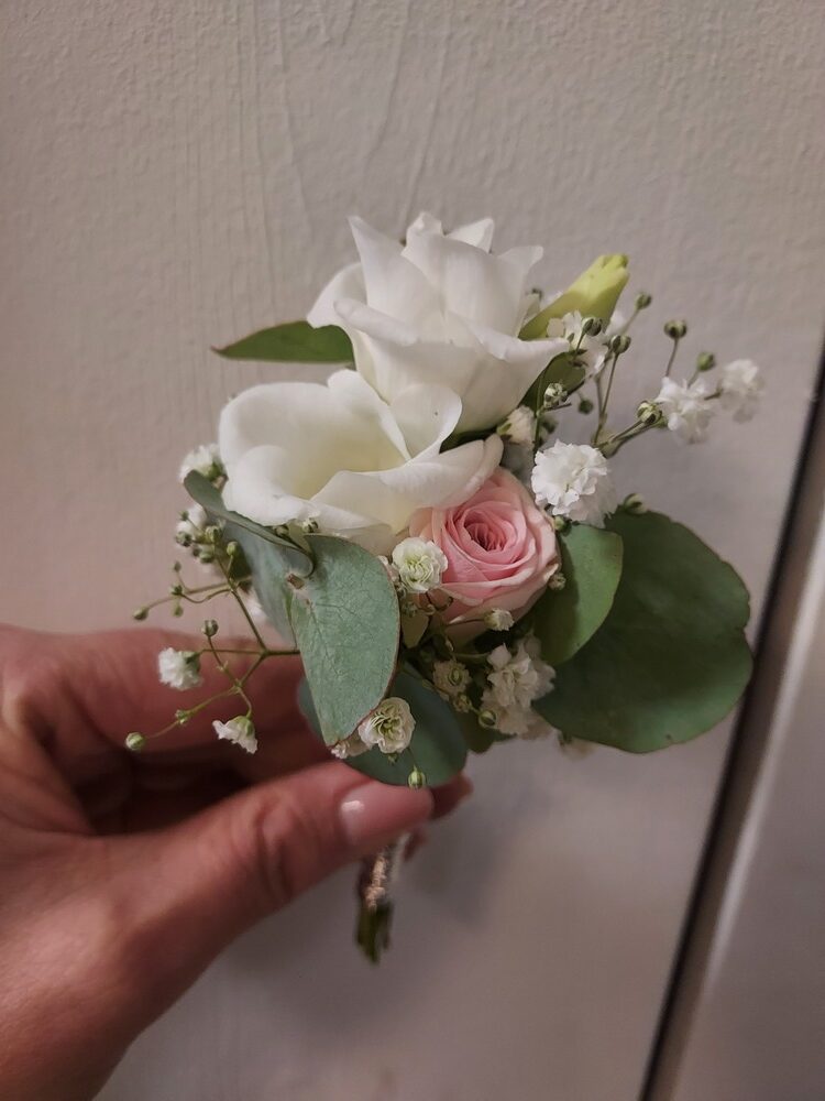 Eine Hand hält ein Blumengebinde mit weißen und rosa Blüten, umgeben von grünen Blättern.