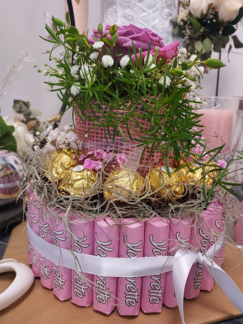 Ein dekorativer Kuchen aus rosa Schokowaffeln, verziert mit goldenen Pralinen und Blumen.