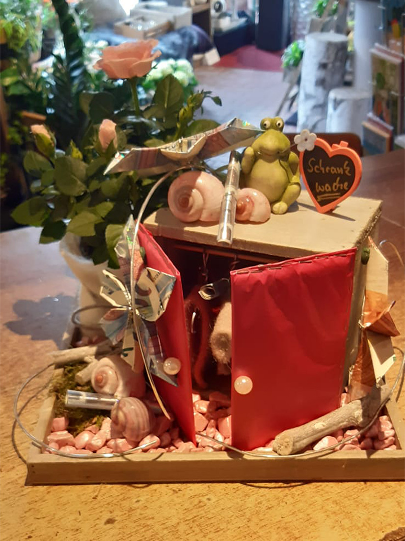 Ein kleines Diorama mit rosa Vorhängen, Schneckenhaus-Deko und grüner Figur.