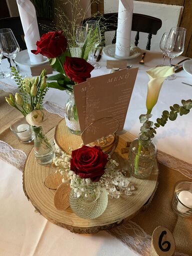 Ein dekorativer Tisch mit roten Rosen, weißen Blumen und einem Holzuntergrund.