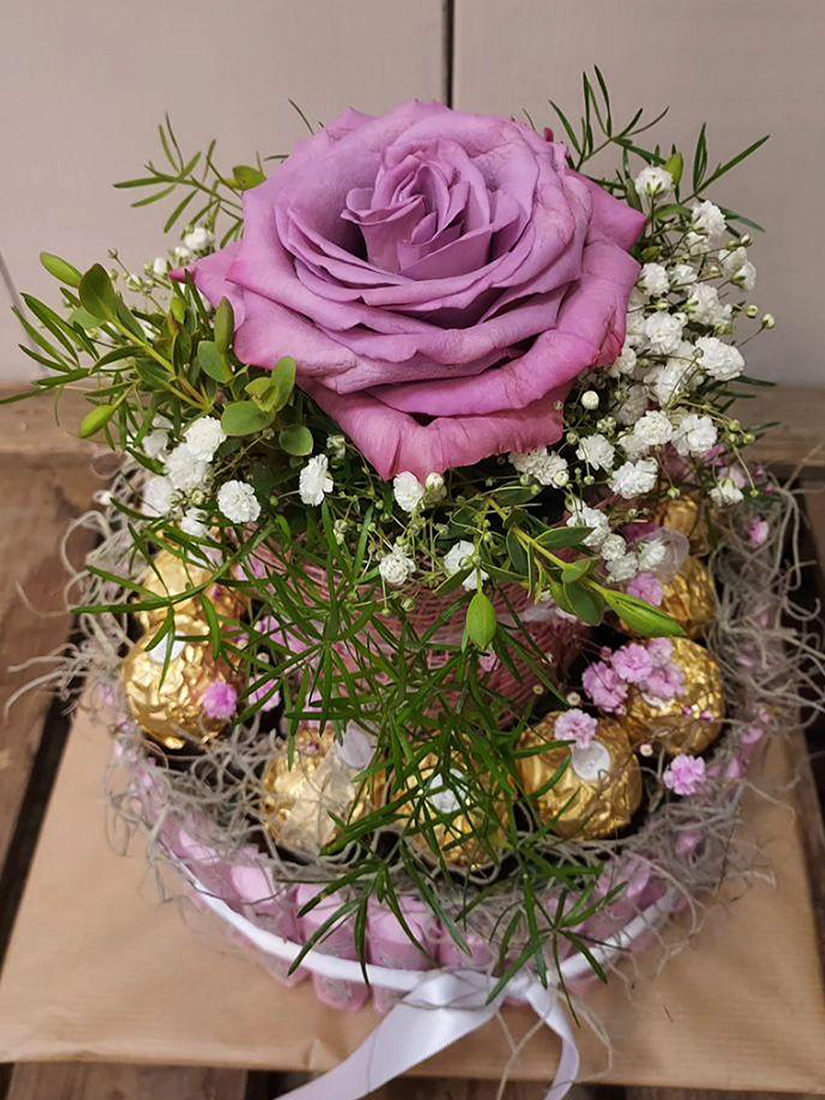 Ein Arrangement mit lila Rose, goldenen Kugeln und zarten weißen Blumen