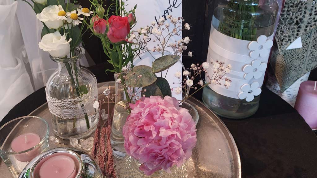 Ein Tisch mit verschiedenen Blumen in Vasen, darunter Rosen und eine große rosa Blüte.