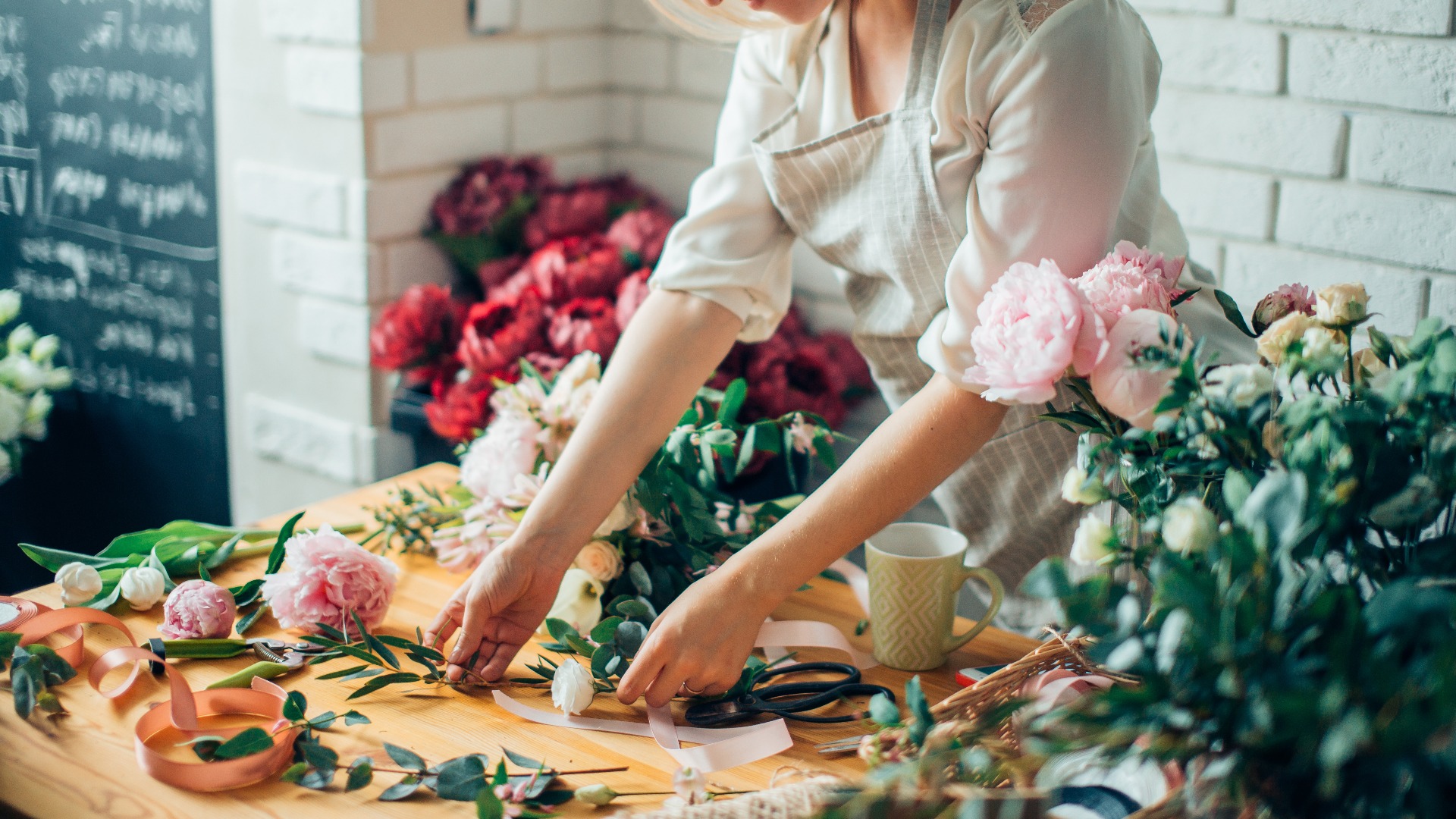 Lächelnde junge Floristin arrangiert Pflanzen im Blumenladen