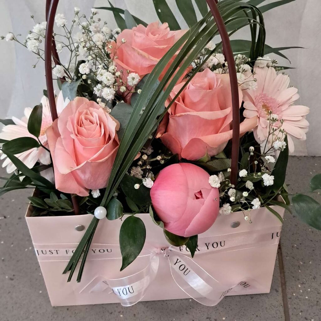 Ein Strauß aus rosa Rosen und weißen Blüten in einer rosa Geschenktasche.
