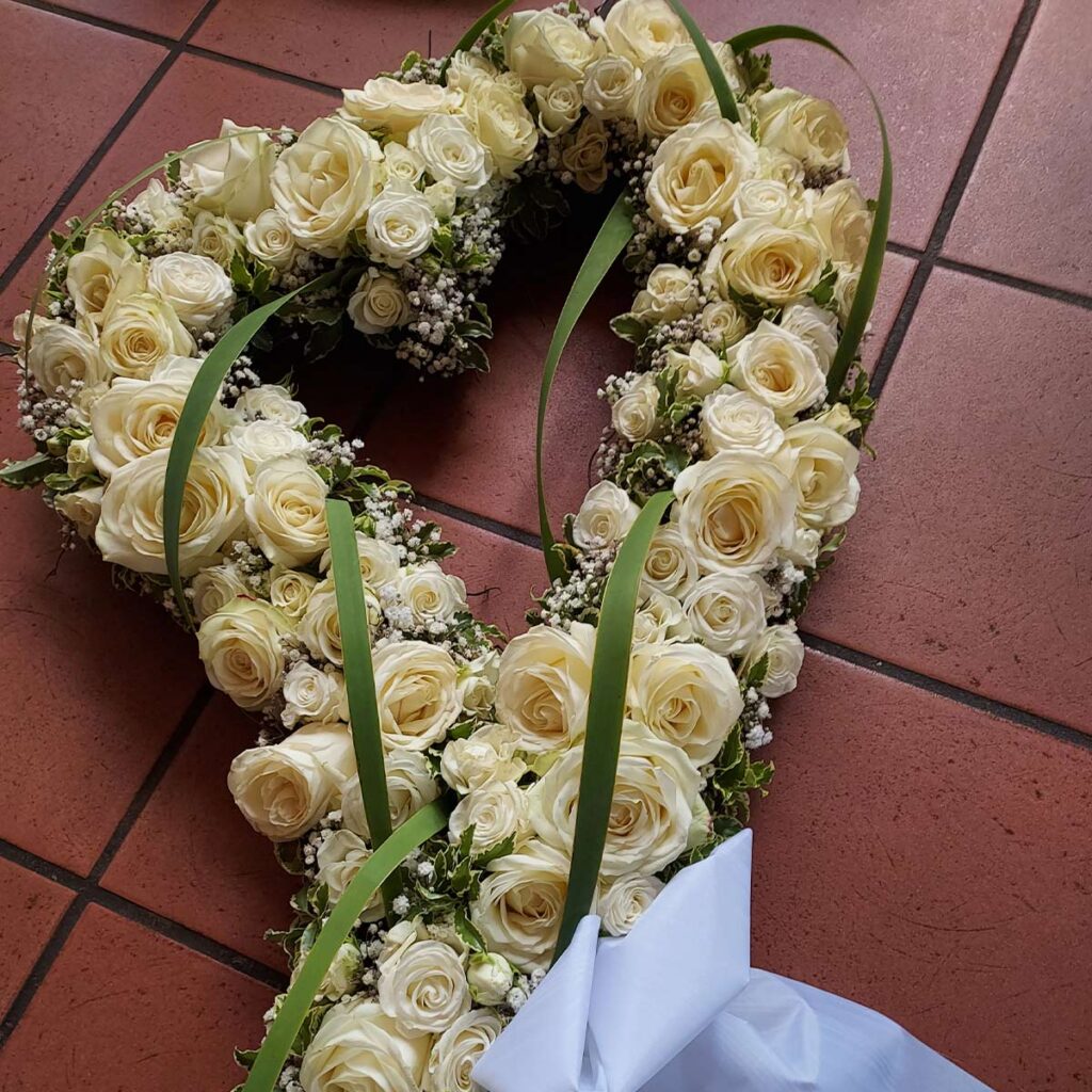 Herzförmiges Blumenarrangement, cremefarbene Rosen mit grünen Blättern auf rotem Boden