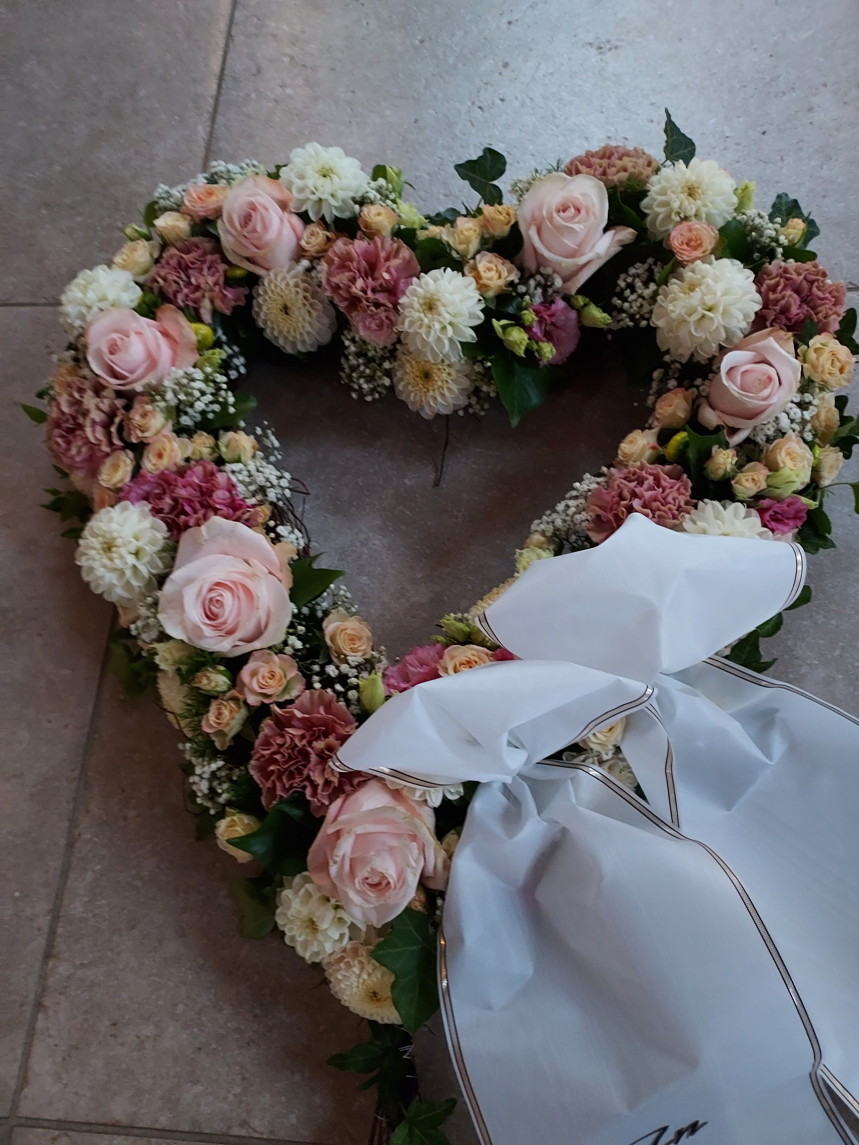 Ein herzförmiges Blumenarrangement aus rosa und weißen Rosen mit Schleife.