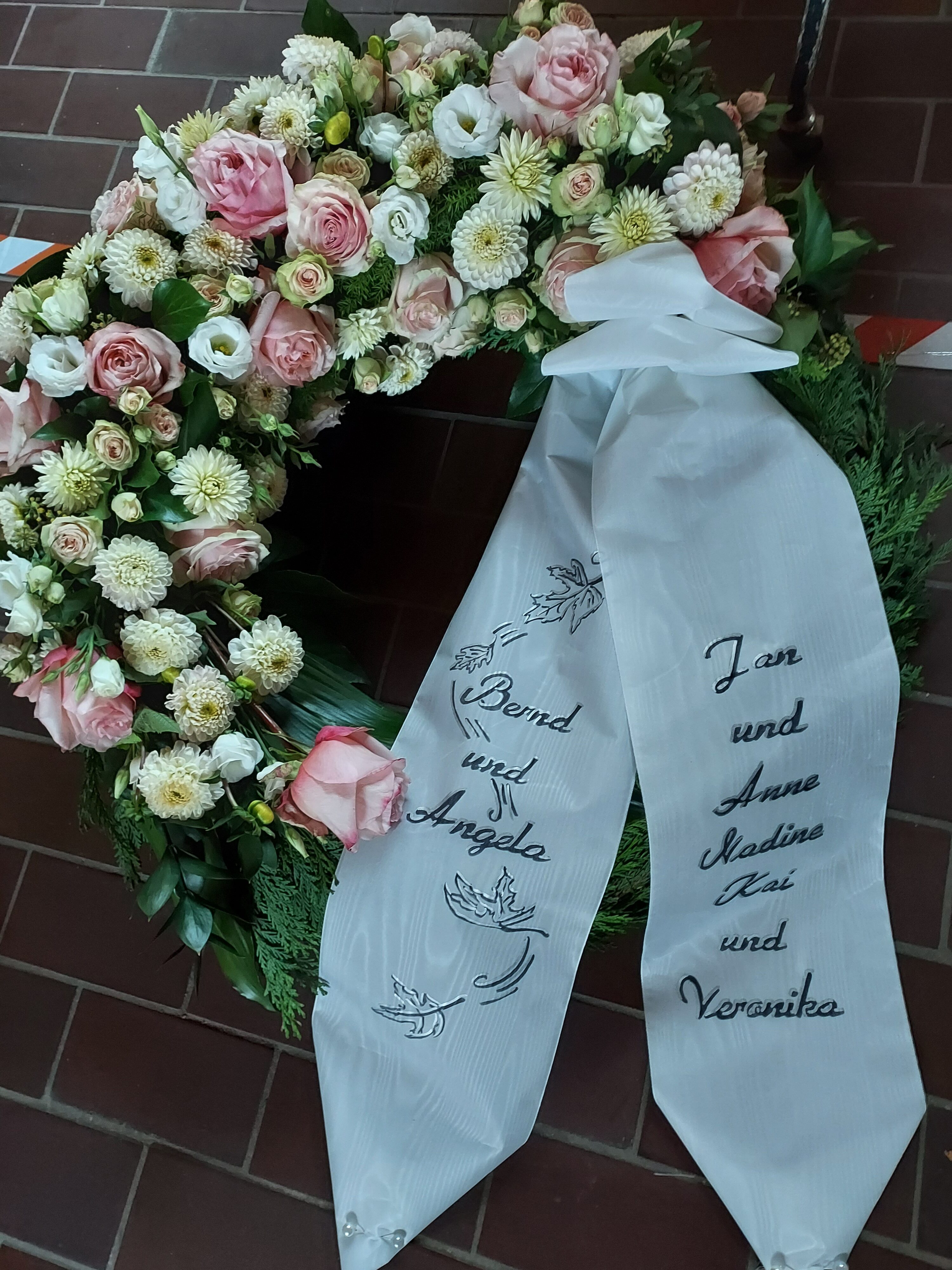 Ein Blumengebinde mit rosa und weißen Blüten und weißen Bändern mit Namen.