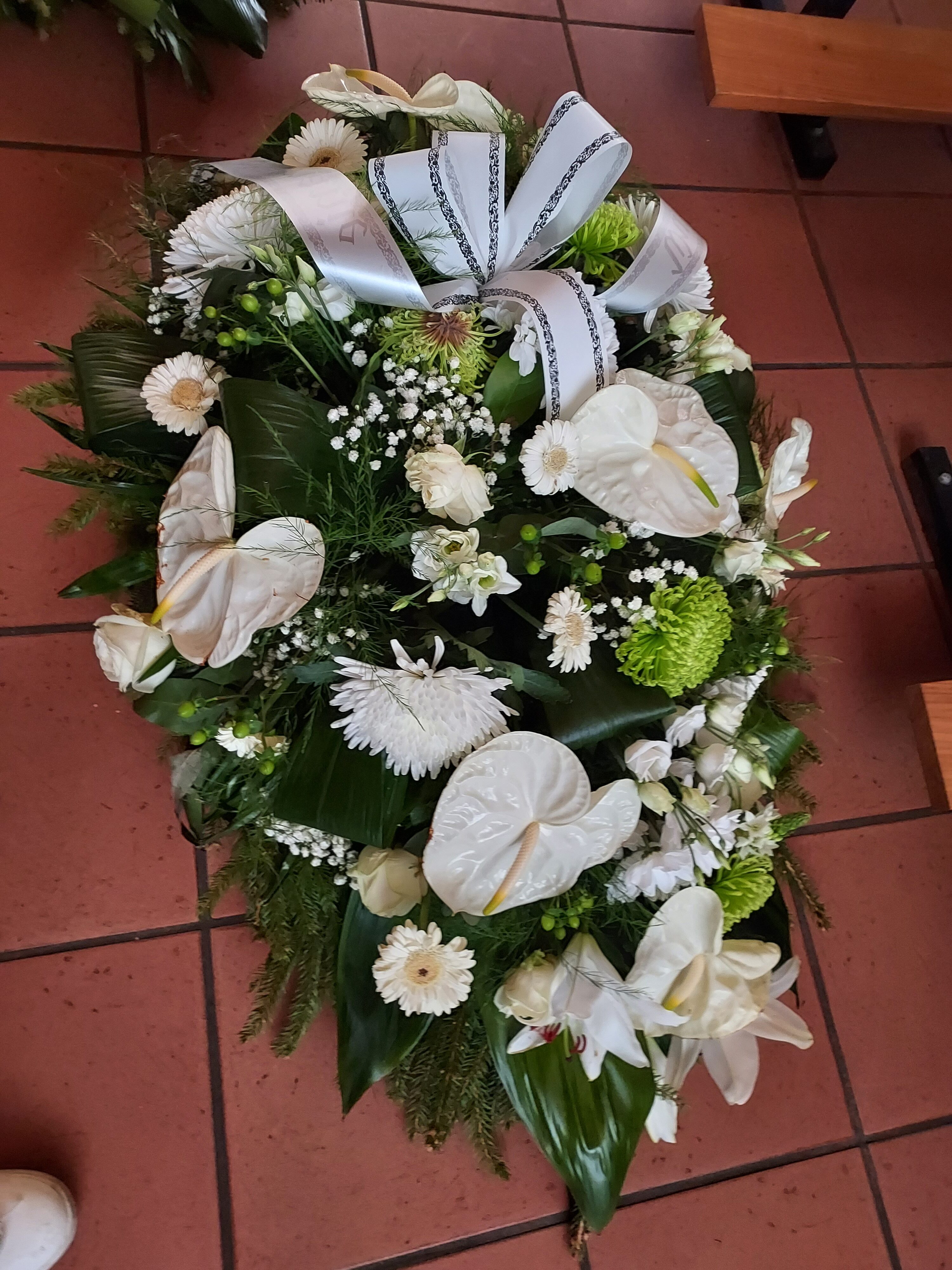 Ein weißer Blumenkranz mit grünen Blättern und dekorativem Band.