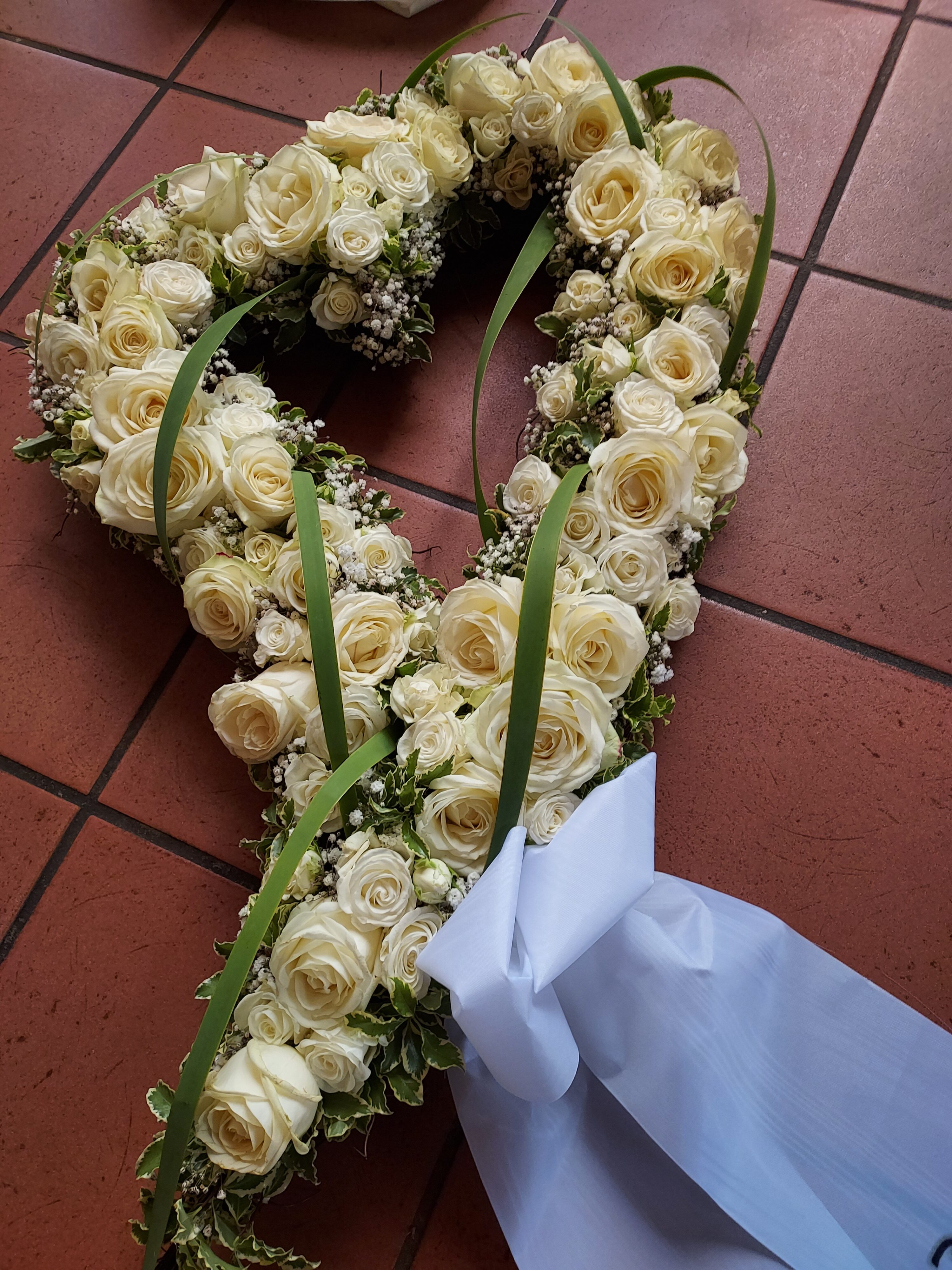 Herzförmiges Blumengesteck aus cremefarbenen Rosen und grünem Laub.