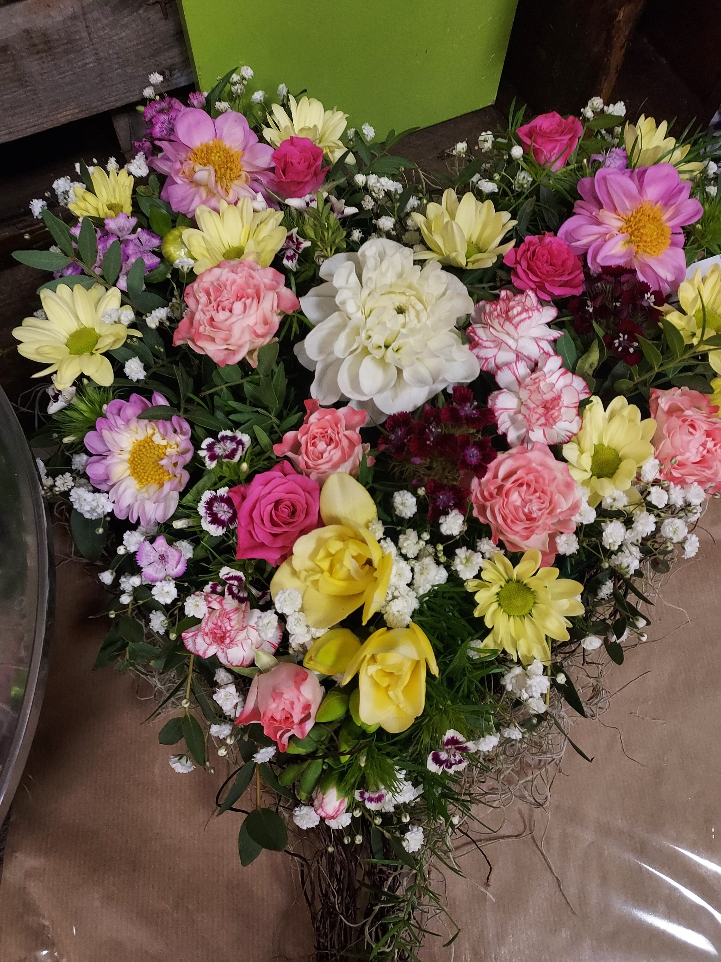 Ein herzförmiges Blumenarrangement mit pinken, gelben und weißen Blüten.