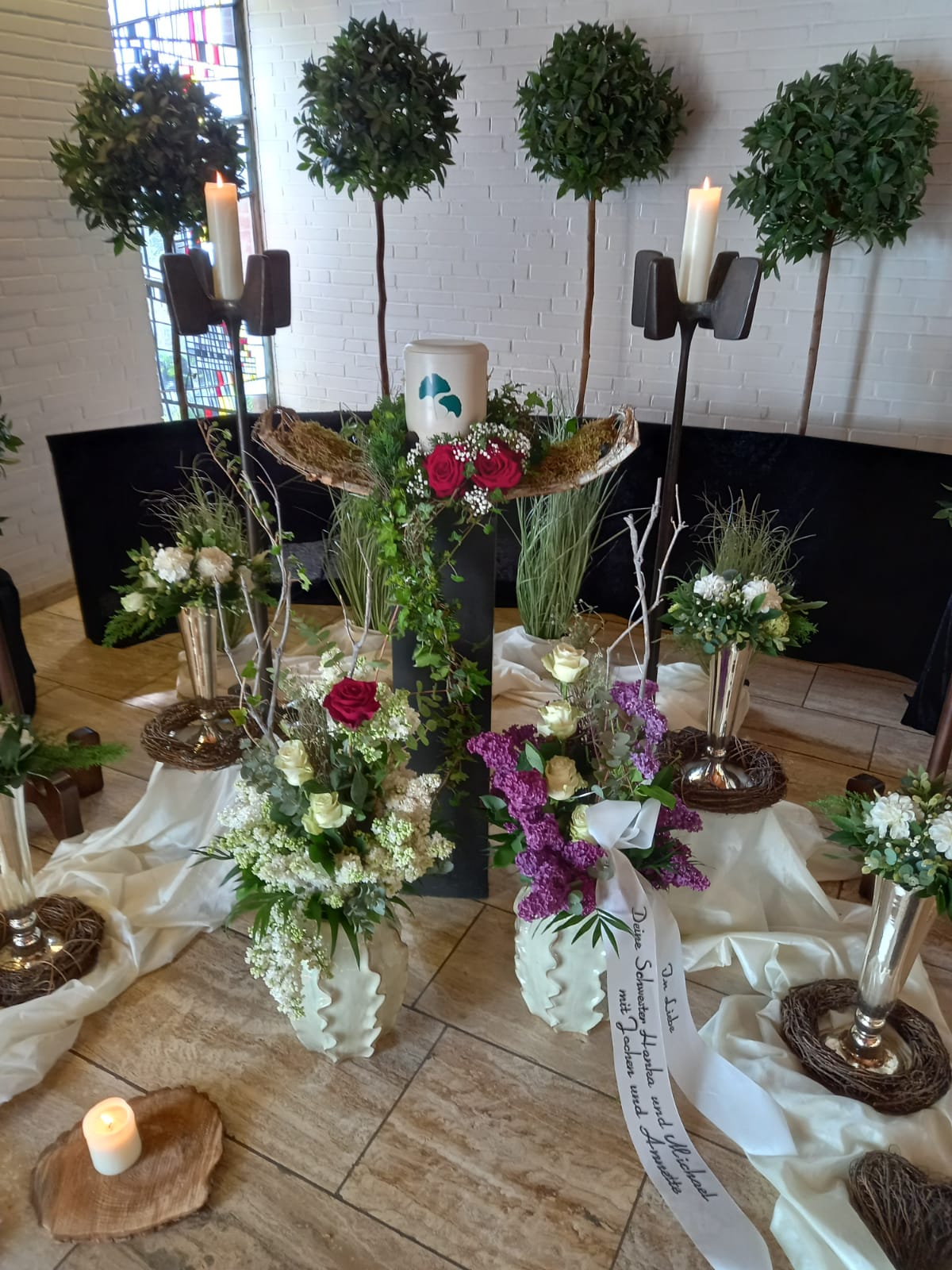 Ein geschmackvoll arrangierter Traueraltar mit Blumen, Kerzen und Kränzen.