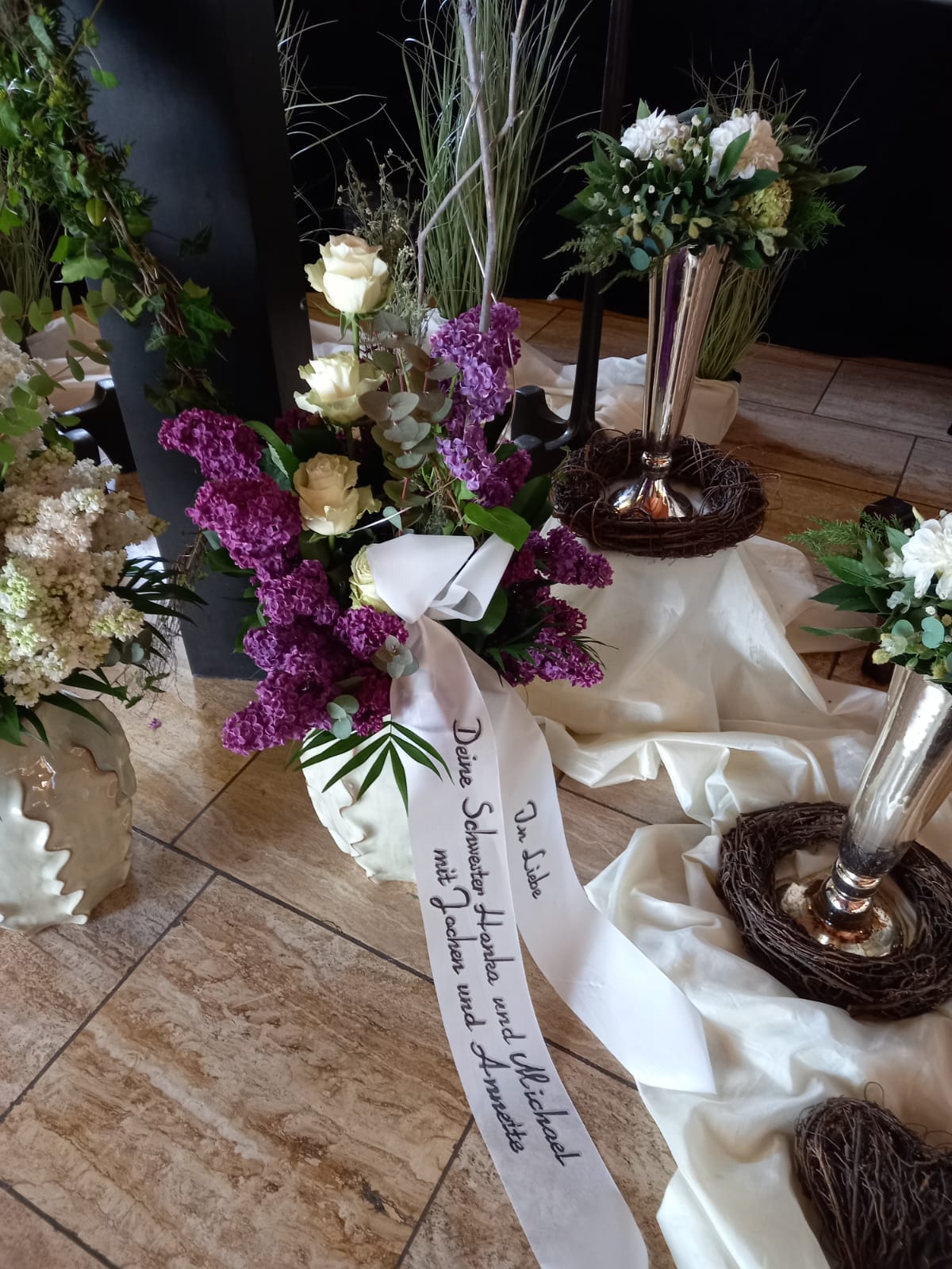 Blumenarrangement mit lila und weißen Blumen, dekoriert mit Schleifenband.