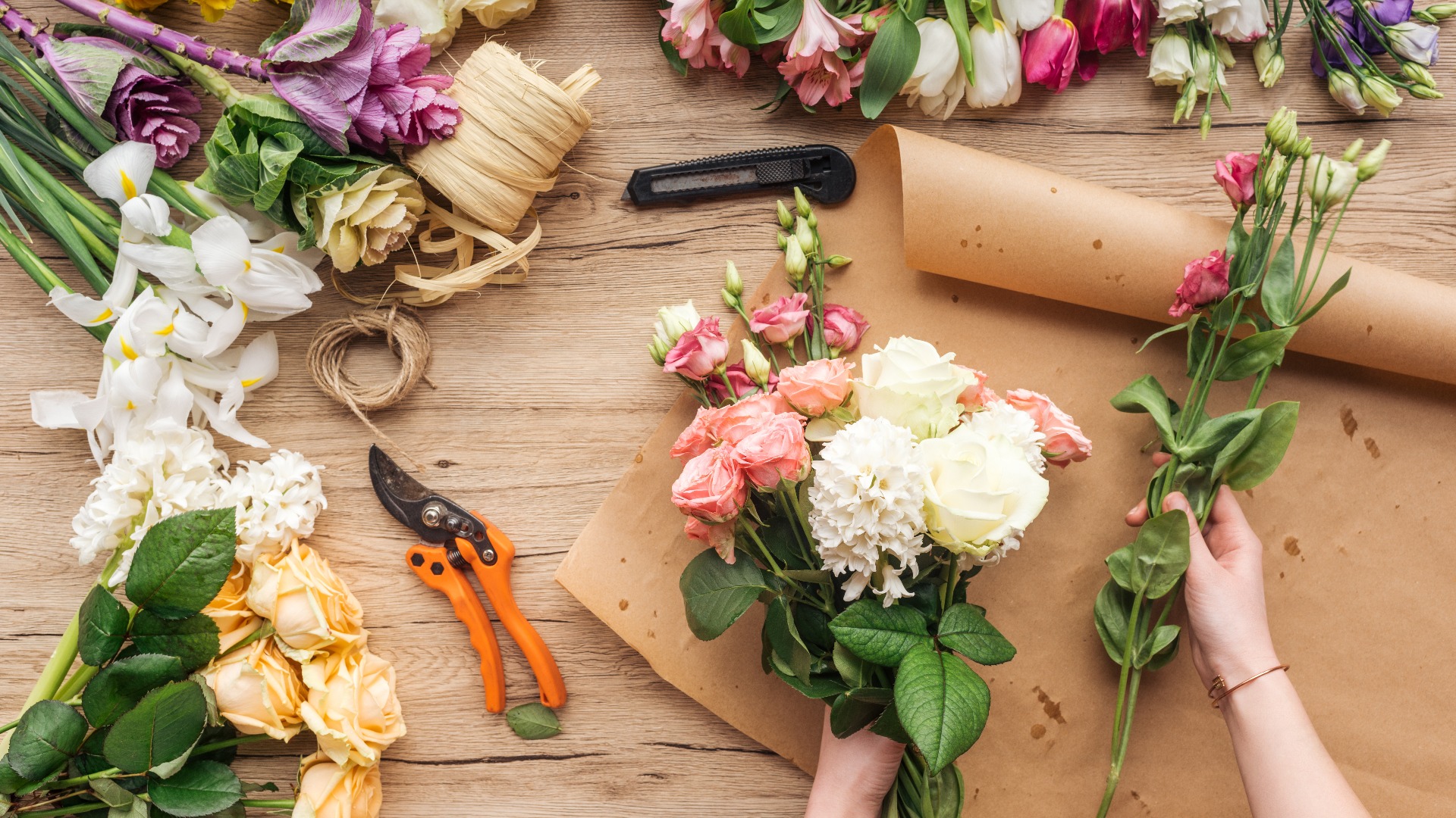 Teilansicht einer Floristin, die einen Blumenstrauß auf einer hölzernen Fläche anfertigt
