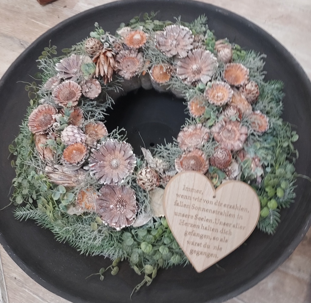 Getrockneter Kranz mit Blumen in Braun und Grün auf schwarzem Teller, Holzh Herz