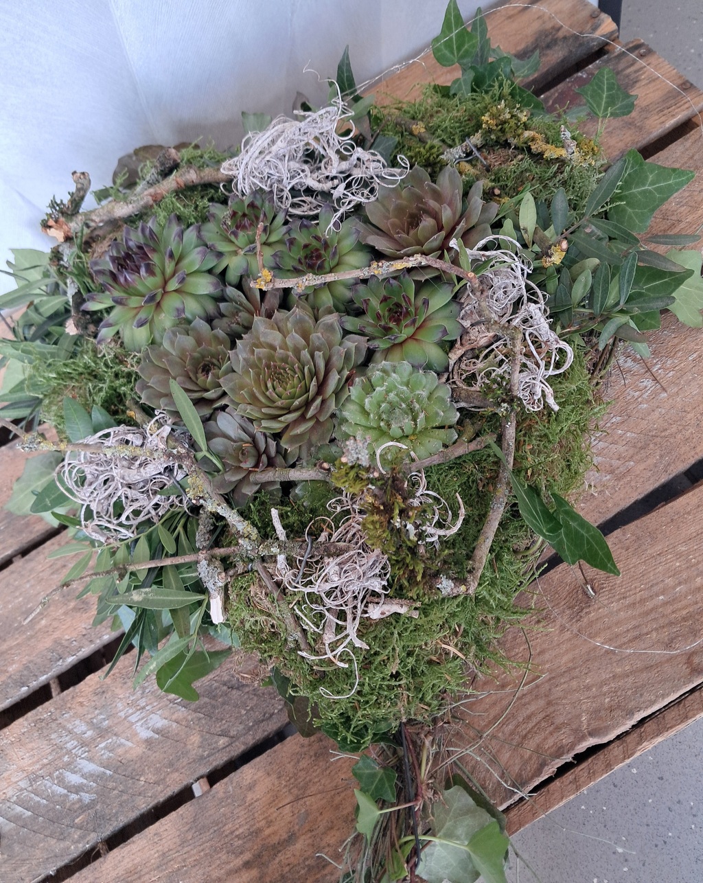 Herzförmiges Arrangement aus Sukkulenten, Moos und Zweigen auf Holzpalette