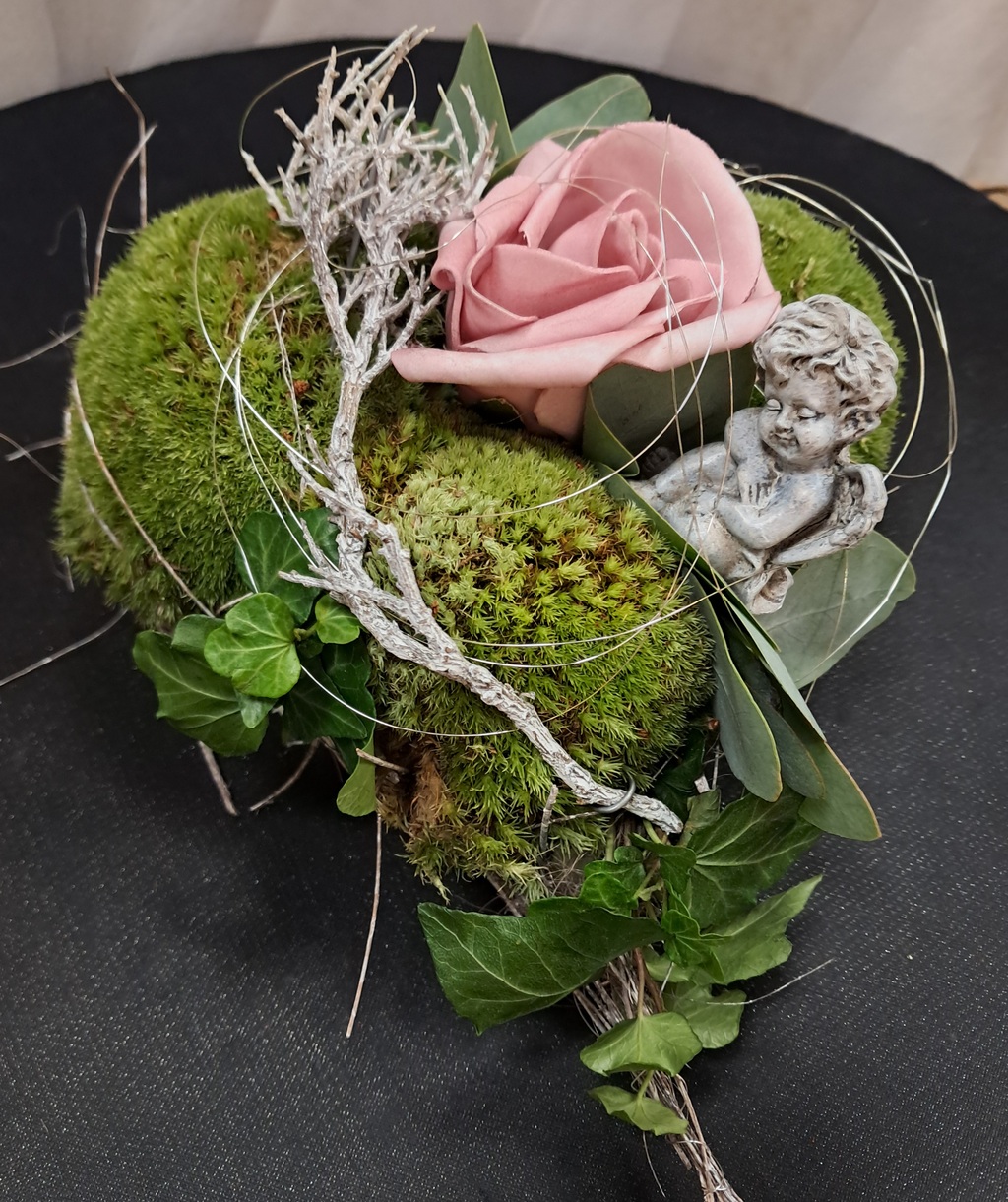 Rosa Rose und Moos mit Efeu geschmückt, daneben eine kleine Engelsfigur mit freundlichem Gesichtsausdruck