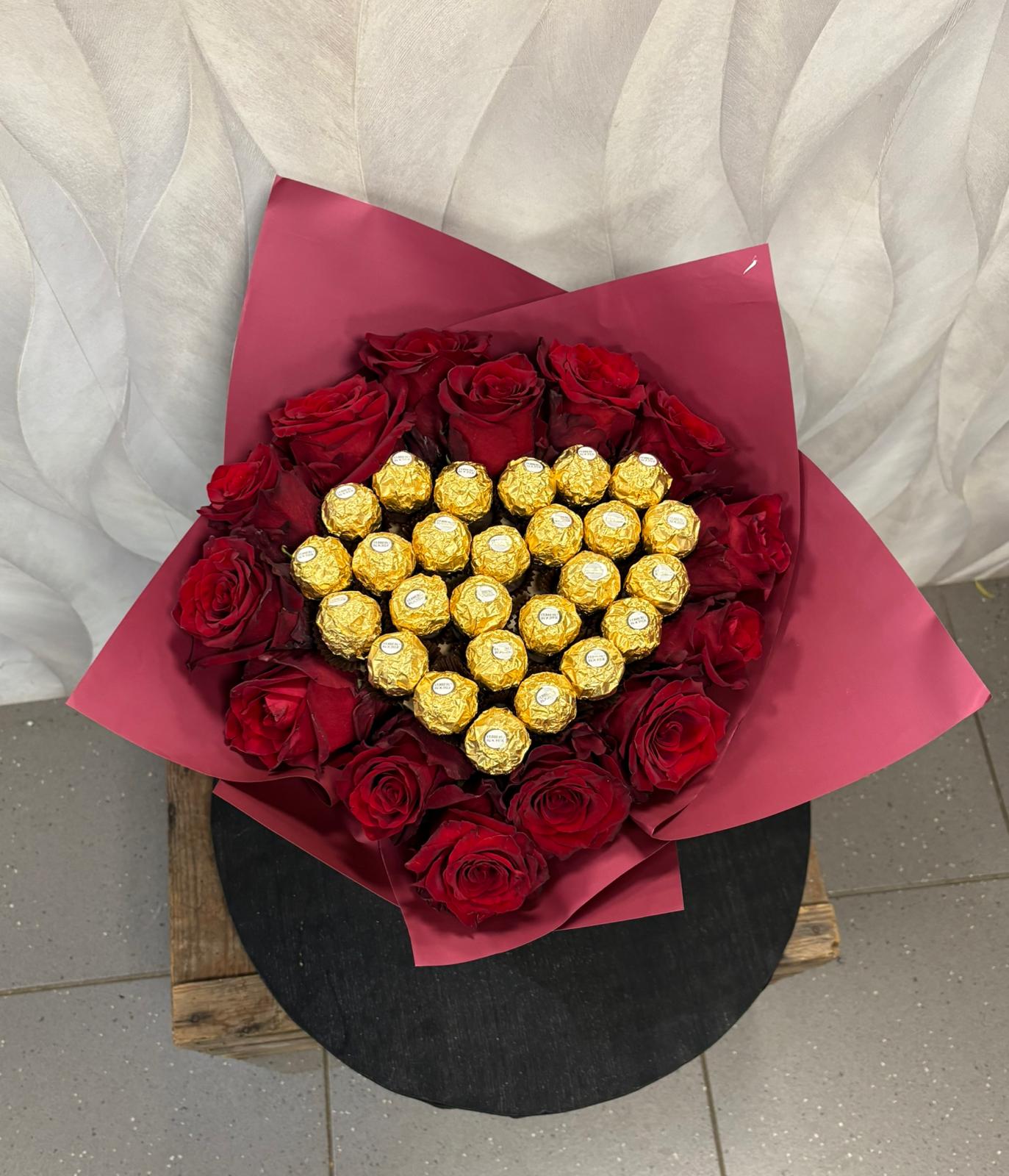 Ein Strauß aus roten Rosen mit goldenen Pralinen in Herzform dekoriert
